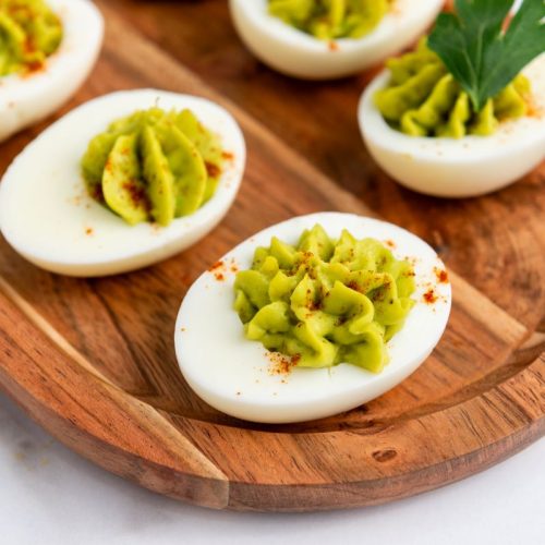 Avocado deviled eggs on a wooden board.