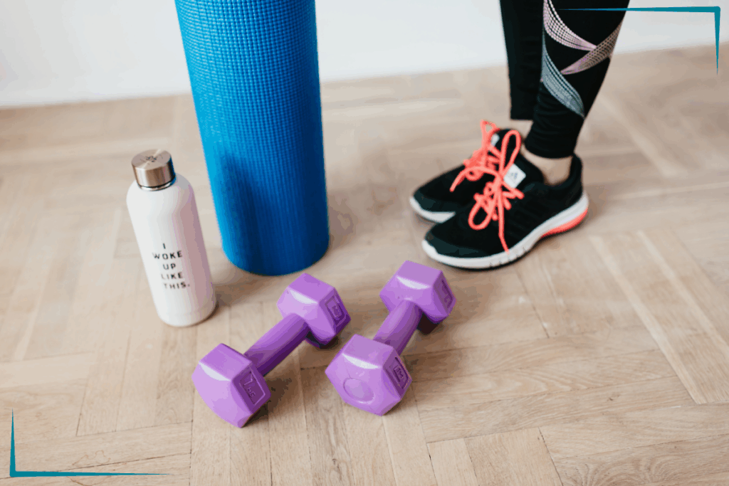 A person standing with weights, a mat and a water bottle.